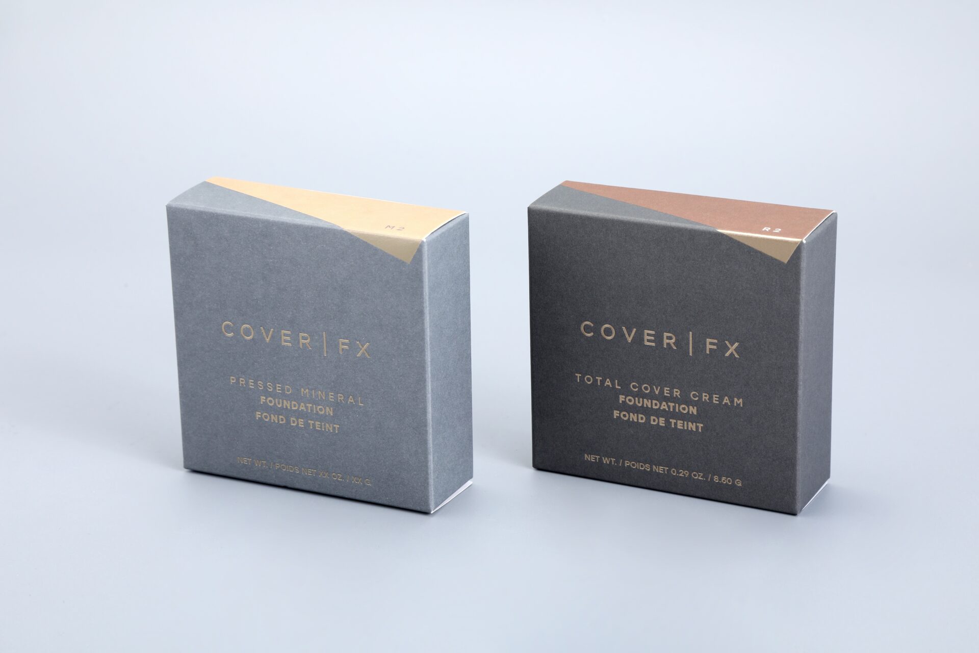 We produce custom packaging solutions. This image showcases our product, featuring two distinct boxes designed for foundation products. One box is tailored for a pressed mineral foundation, while the other is crafted to house a total cover cream foundation, all set against a sleek gray backdrop.