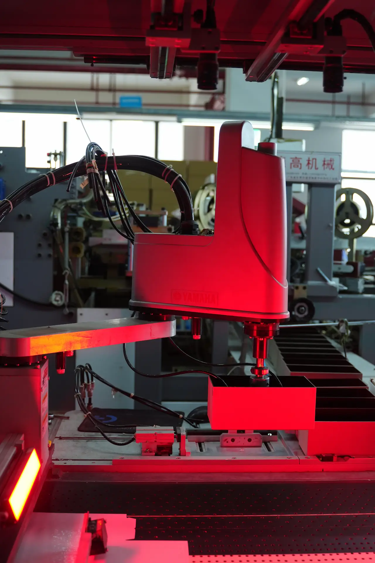 A close-up of an automated machine at the Witpax factory processing small grey paper boxes on a conveyor belt, illuminated by a red light element.