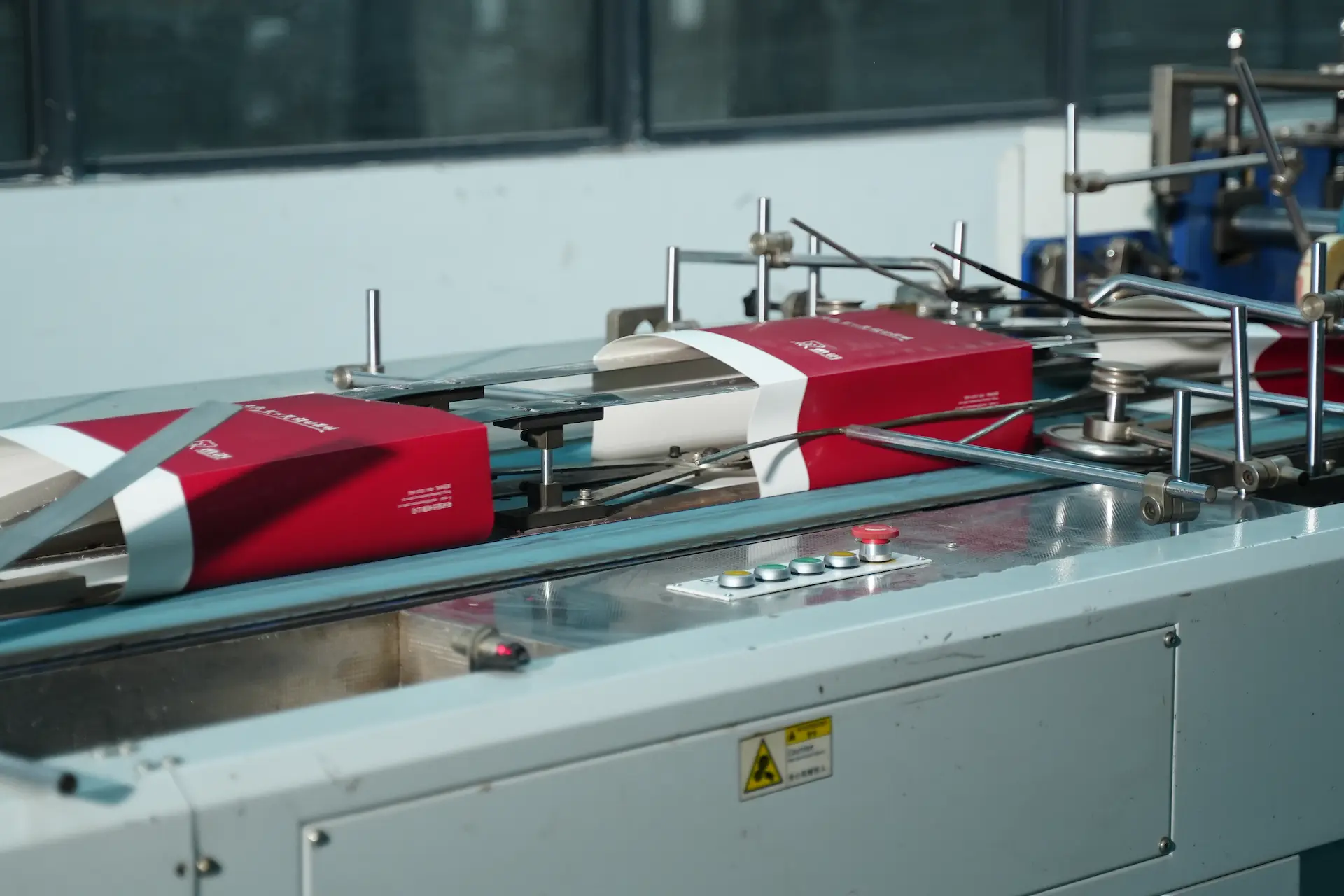 A high-speed automatic folding and gluing machine at the Witpax factory precisely folding flat red paper cartons as they move along a conveyor line.
