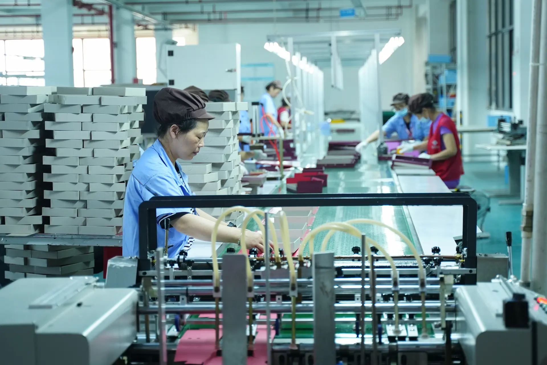 A Witpax factory worker operates an automatic gluing machine on the paper box production line, with stacks of finished boxes nearby.