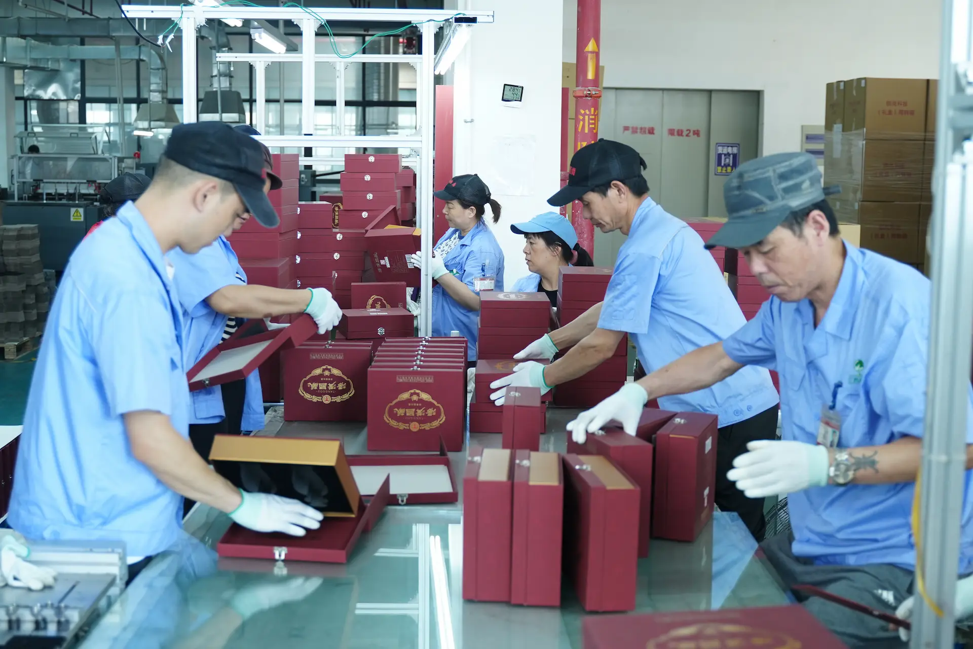 A team of Witpax workers wearing white gloves meticulously hand-assembles and inspects premium red and gold rigid gift boxes at a finishing station.