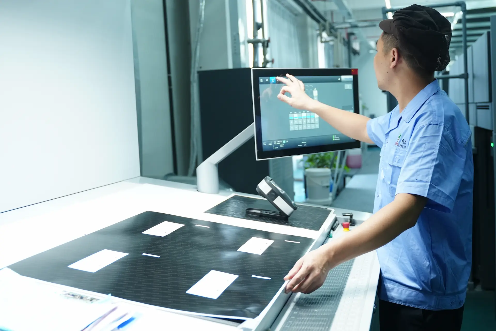 A Witpax factory technician in a blue uniform operates a large touchscreen control panel to calibrate an industrial printing press for paper packaging.