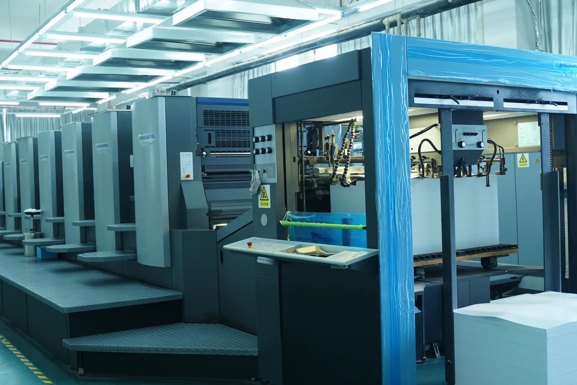 A view of the large, multi-station Heidelberg offset printing press line inside the Witpax factory, with paper stock ready for a high-volume packaging run.
