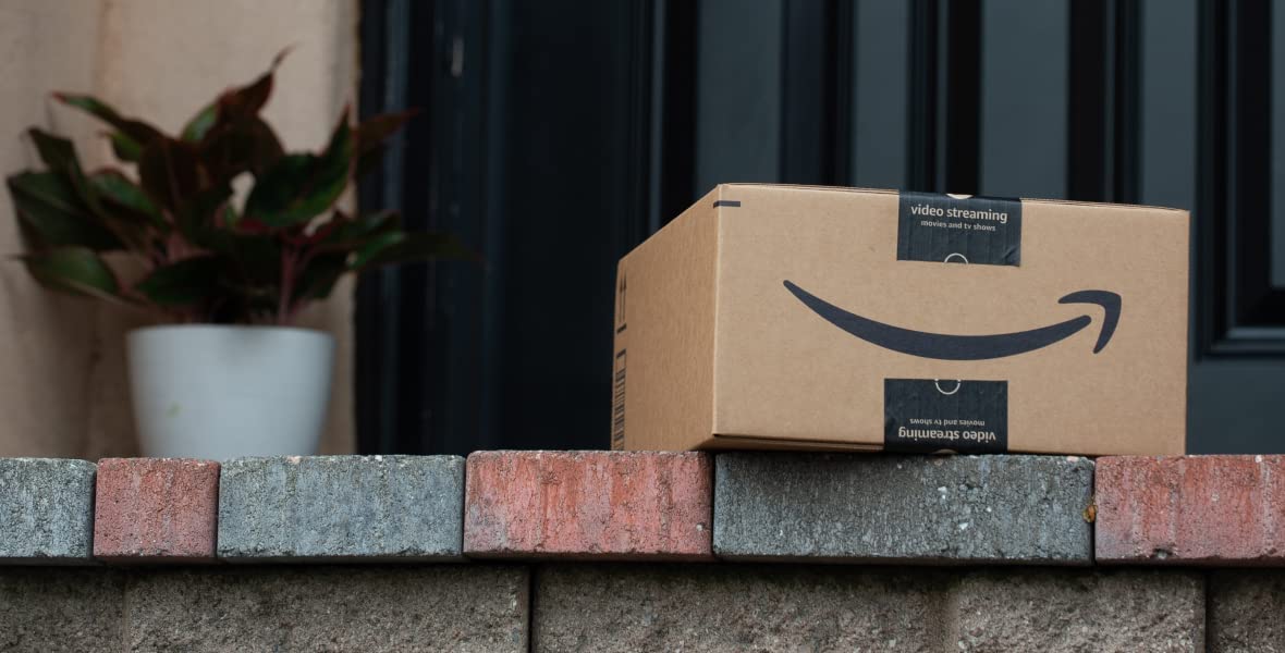 A custom packaging box is placed on a brick ledge in front of a black door, accompanied by a potted plant on the left side.