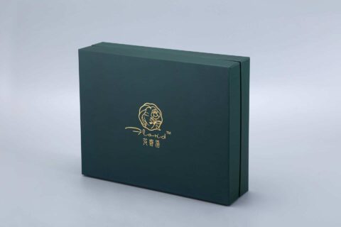 A dark green rectangular gift box featuring a gold logo on the front, set against a light gray background.