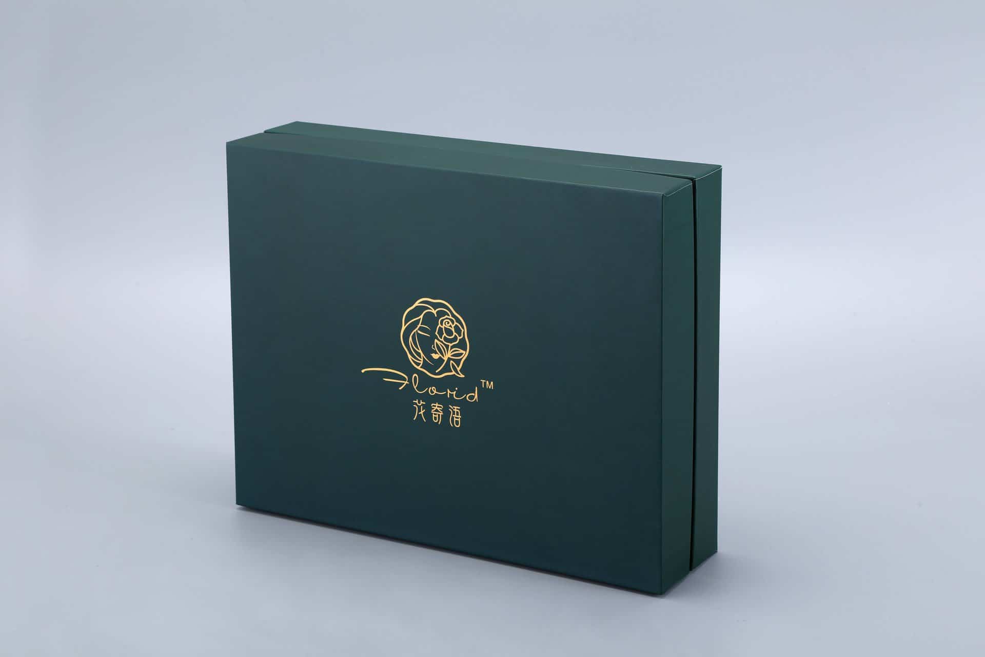 A dark green rectangular gift box featuring a gold logo on the front, set against a light gray background.