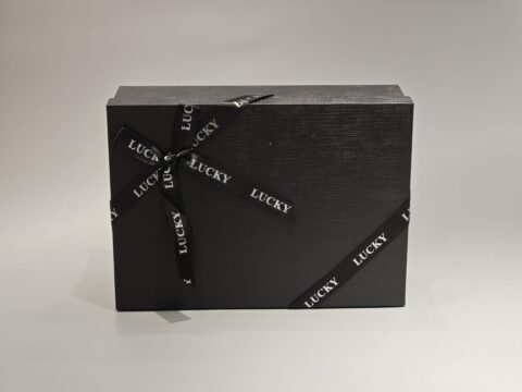 A sleek, custom gift box featuring a dark lift-off lid is elegantly wrapped in a branded ribbon designed with a sophisticated pattern.