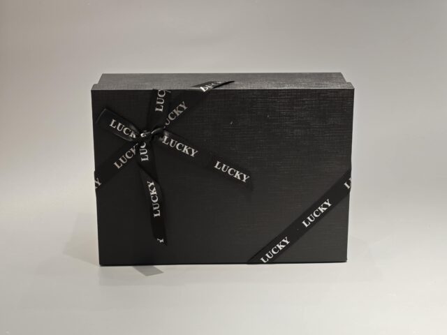 A sleek, custom gift box featuring a dark lift-off lid is elegantly wrapped in a branded ribbon designed with a sophisticated pattern.