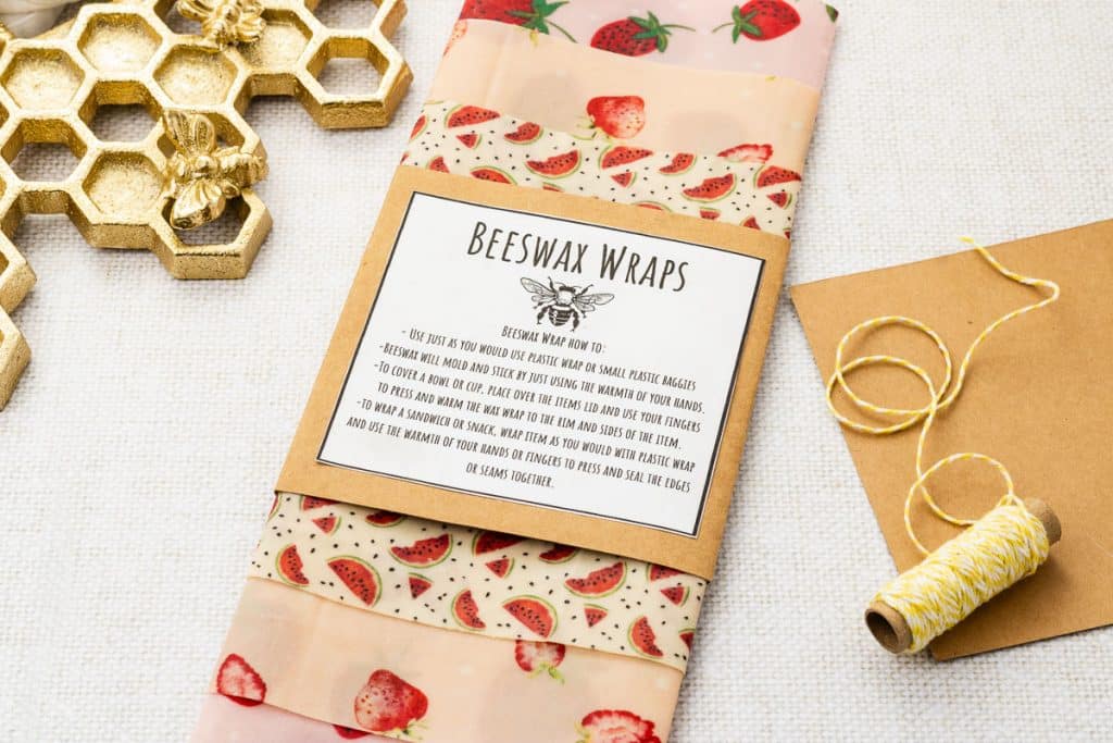 Eco-friendly beeswax wraps with a strawberry pattern, instructions, and twine on a white surface.
