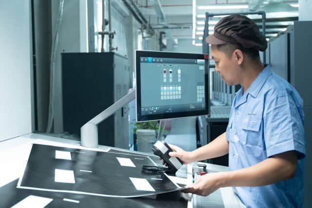 Person inspecting printed materials at a workstation with a computer monitor.