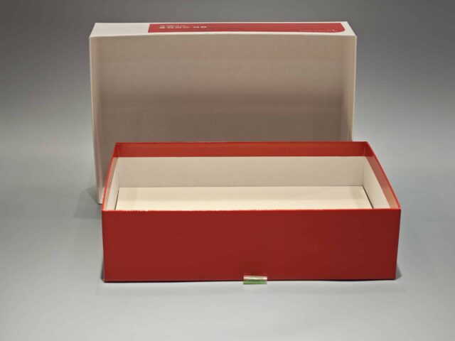 The product is a custom box packaging for a Korean Red Ginseng with Pomegranate product. The box features vibrant and detailed illustrations of ginseng roots and pomegranate fruits, giving it an appealing and eye-catching design. The overall color scheme complements the images, set against a gray surface that enhances the vividness of the artwork. This bespoke packaging highlights both traditional and contemporary aesthetics, reflecting the premium quality of its contents.