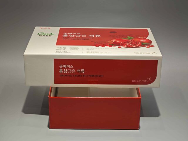 The product is a custom box packaging for a Korean Red Ginseng with Pomegranate product. The box features vibrant and detailed illustrations of ginseng roots and pomegranate fruits, giving it an appealing and eye-catching design. The overall color scheme complements the images, set against a gray surface that enhances the vividness of the artwork. This bespoke packaging highlights both traditional and contemporary aesthetics, reflecting the premium quality of its contents.